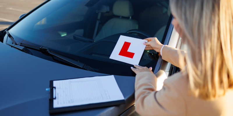 Woman placing an L-plate onto a car windscreen