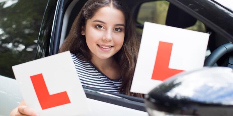 Girl smiling in drivers seat and holding up 'L' plates